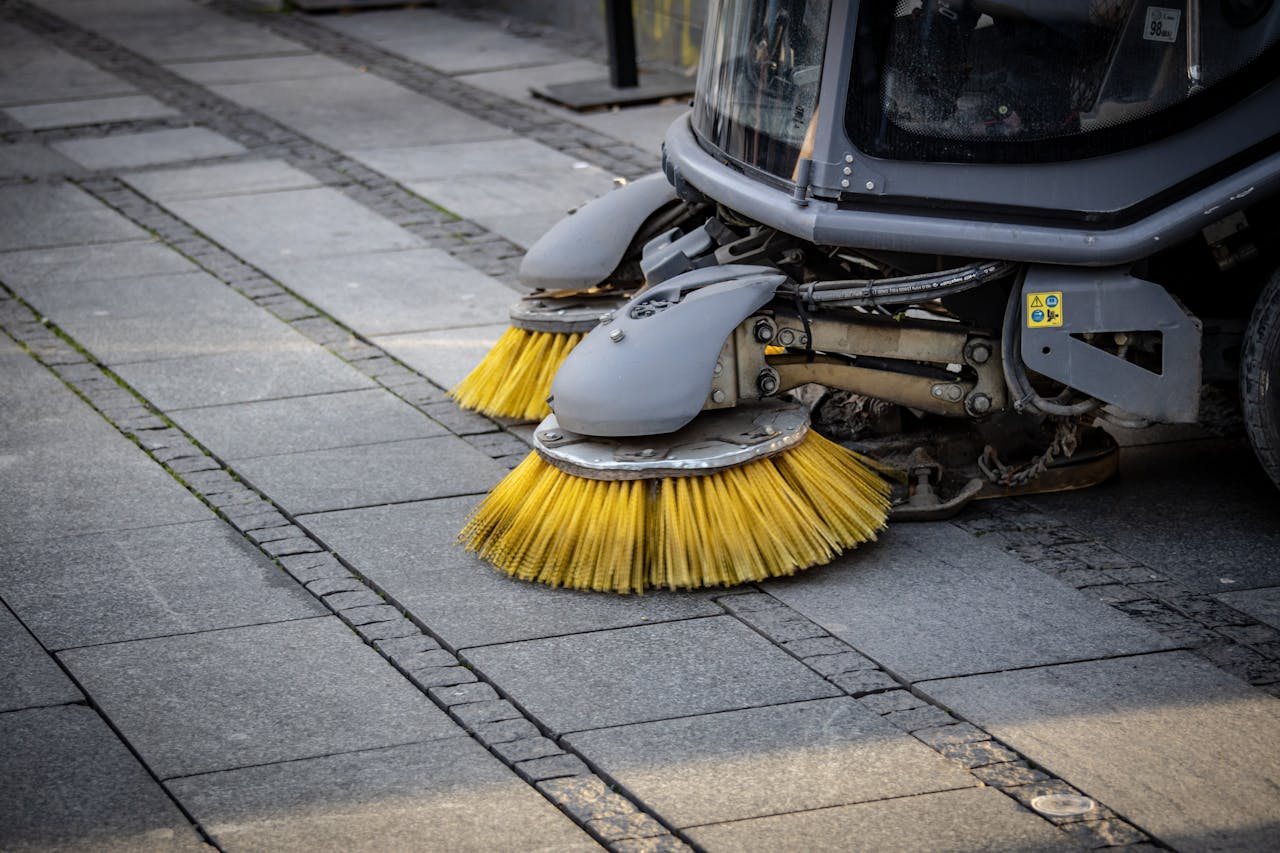 services-02 Close-up view of a road sweeper's yellow brushes on a paved street.