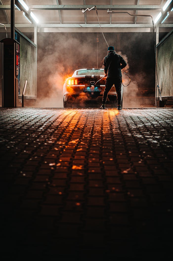 gallery-5 A person washing a sports car at a carwash during the night, illuminated by lights.