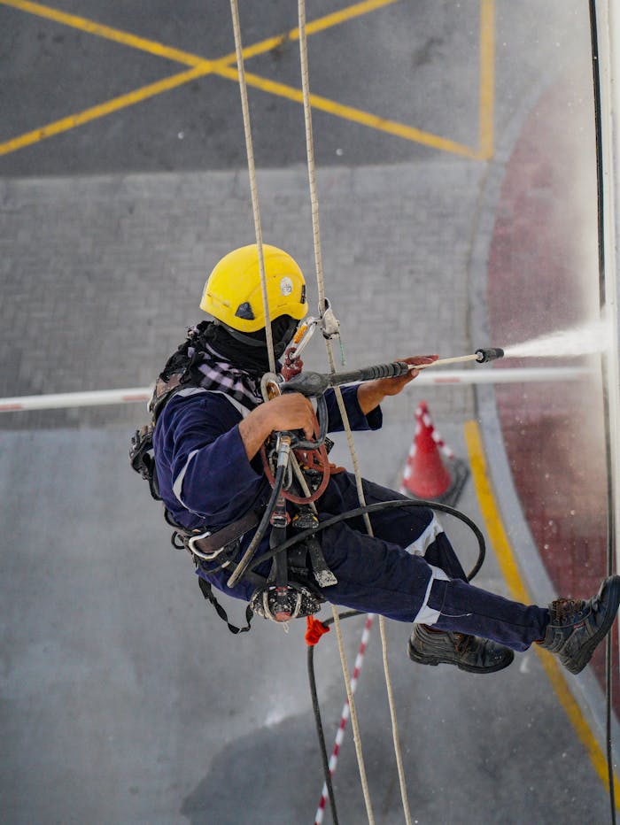 about-01 A worker in safety gear high up cleaning a building with a pressure washer in Dubai.