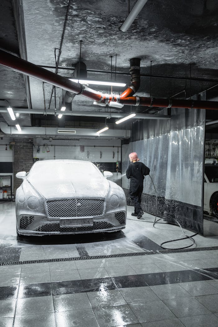 gallery-3 A person washes a luxury car indoors using a pressure washer. Modern automotive care scene.